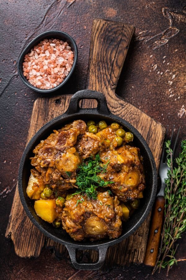 Beef oxtails stew with wine and vegetables in a pan. Dark background. Top view