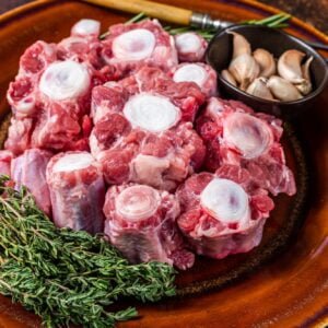 Fresh uncooked beef Oxtail cut Meat on rustic plate with herbs. Dark background. Top view