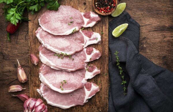Raw pork chops on rustic wooden cutting board prepared for cooking with garlic, thyme, spices