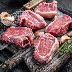 Fresh Raw lamb loin chops steaks, cutlets on butcher board with meat cleaver.
